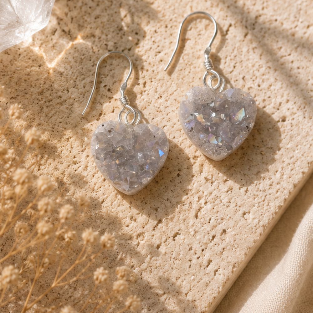 Heart-shaped earrings on a textured beige surface with dried flowers.