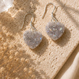 Heart-shaped earrings on a textured beige surface with dried flowers.