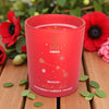 Red candle with Aries zodiac design on a wooden surface with flowers in the background