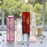 Love Roll-Ons plus a rose quartz tumble on a table with a blurred green outdoor background