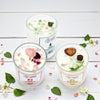 Three scented candles with decorative elements on a white wooden surface with flowers and leaves.