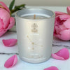 Candle in a silver container with 'Cancer' design, surrounded by pink flowers and petals on a marble surface.
