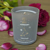 Candle with Capricorn design surrounded by pink roses on a wooden surface