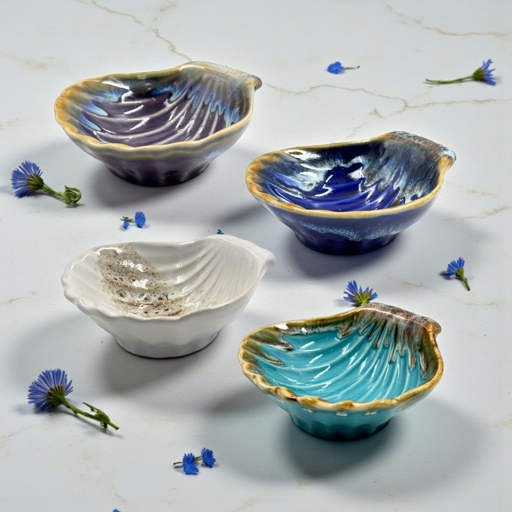 Four ceramic bowls in different colors on a marble surface with small flowers.