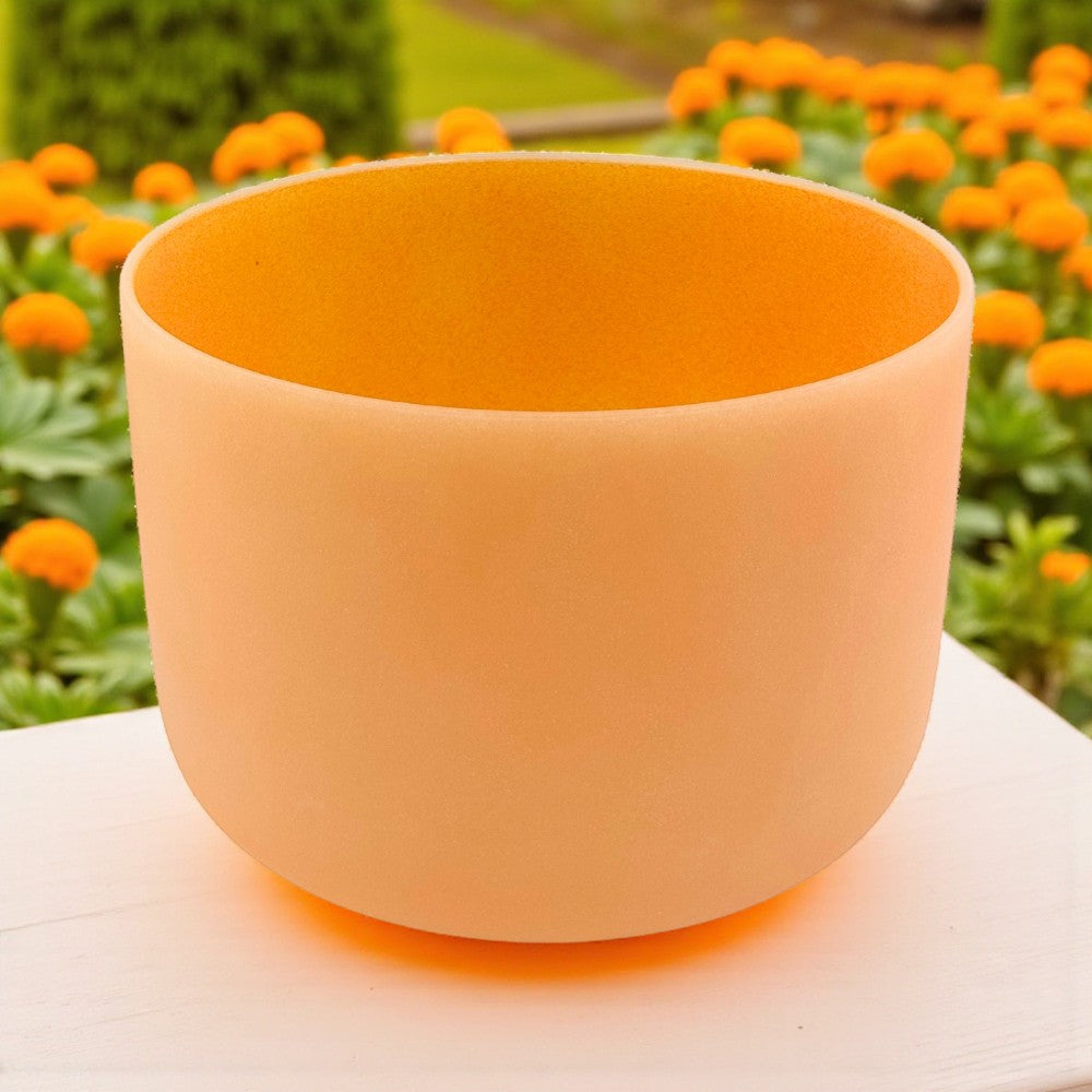 Chakra Crystal Singing Bowl - Sacral on a white surface with flowers in the background