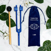 Blue tuning fork with wooden handle and blue pouch on a marble surface with leaves and flowers.