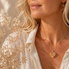 Woman wearing a necklace with a heart-shaped pendant in front of dried flowers