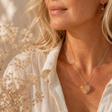 Woman wearing a necklace with a heart-shaped pendant in front of dried flowers