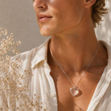 Person wearing a necklace with a heart-shaped pendant in a natural setting