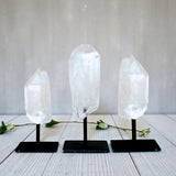 Three Clear Quartz Point on Metal Base on stands against a white background