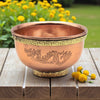 Copper bowl with dragon design on a wooden surface with yellow flowers in the background