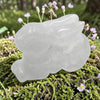 Clear quartz bunny on a green mossy surface with small purple flowers