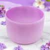 Purple crystal bowl on a marble surface with purple flowers.