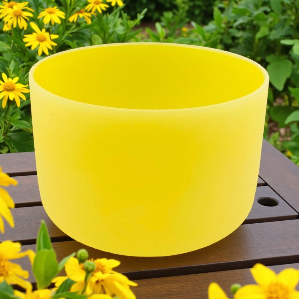 Chakra Crystal Singing Bowl - Solar Plexus on a wooden surface with yellow flowers in the background