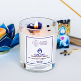 Candle in a glass jar with a label on a white surface, surrounded by decorative items.