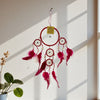 Red and pink dreamcatcher hanging on a white wall with a plant in the corner.