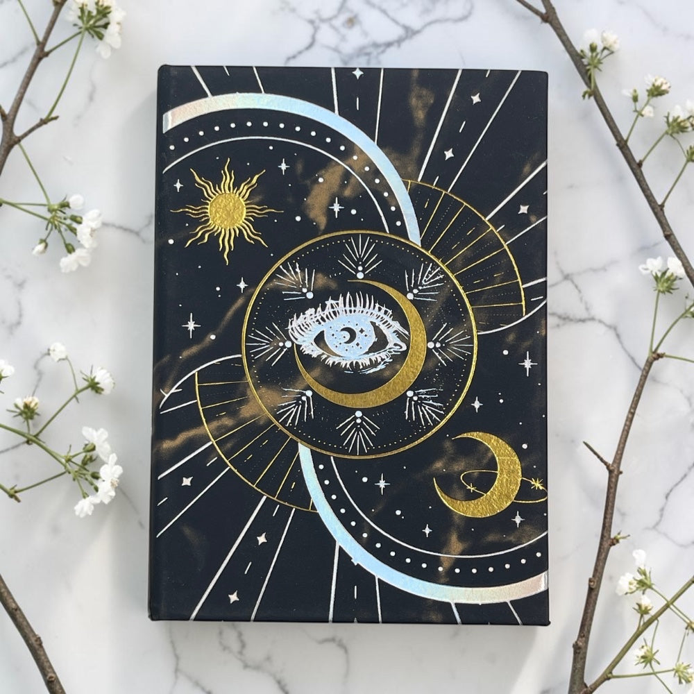 Decorative journal with celestial design on a marble surface with white flowers and branches.