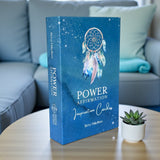 Blue box of 'Power Affirmation Inspiration Cards' with a dreamcatcher design on a table with a couch and plant in the background.