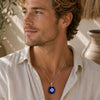 Man wearing an Evil Eye Glass Pendant on a delicate silver chain with a cream linen shirt.