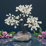 Decorative crystal tree on a rock with pink roses against a dark background