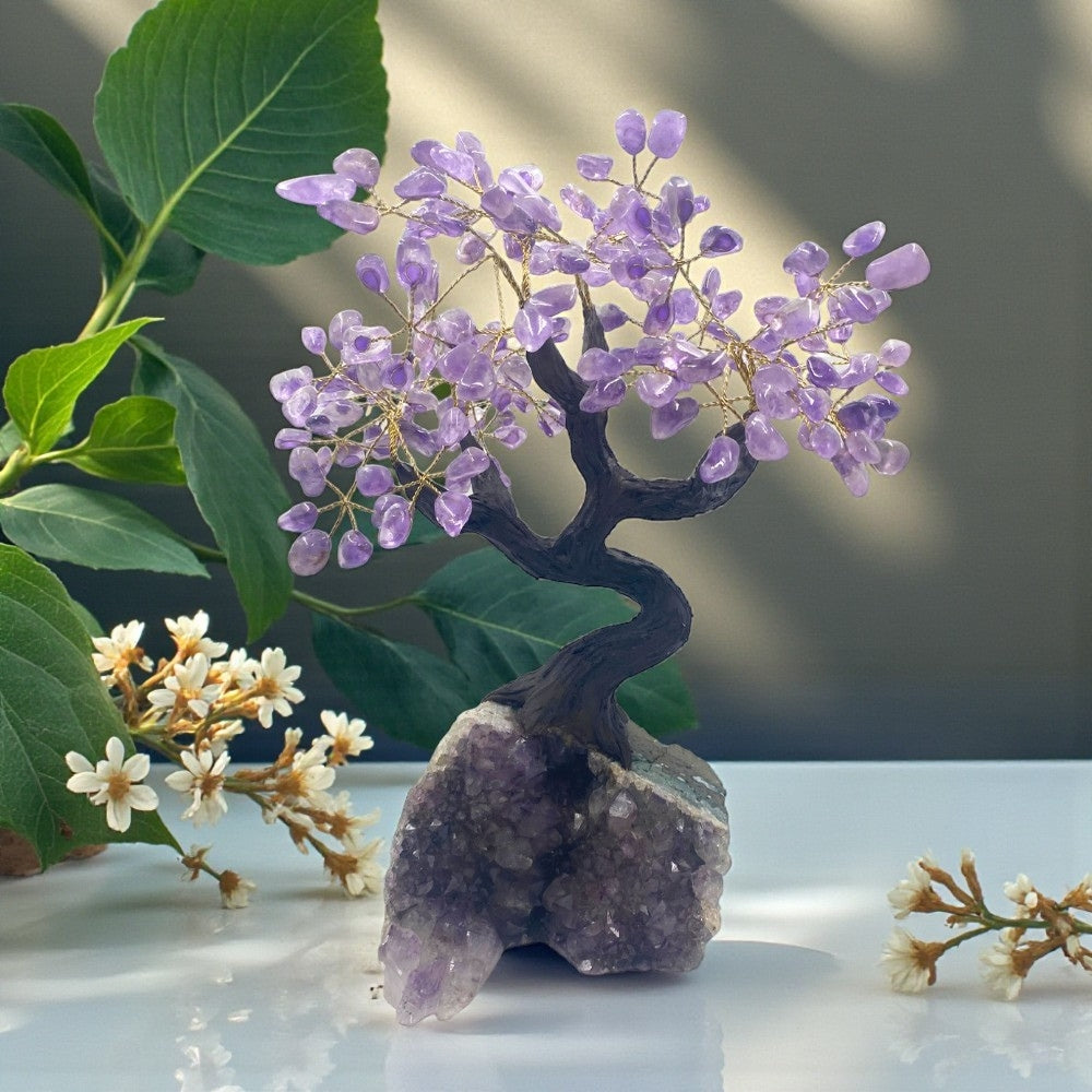 Decorative amethyst  crystal tree on a rock with green leaves and white flowers in the background