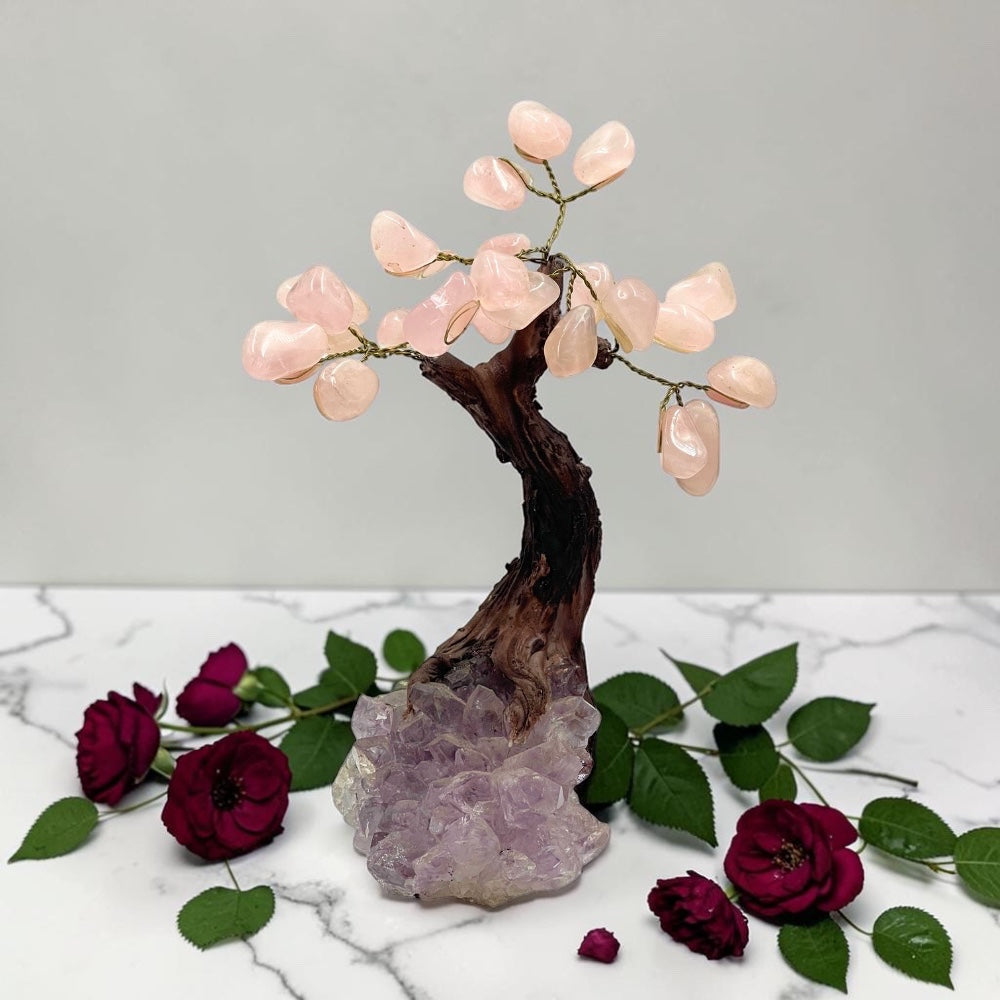 Decorative stone tree with pink stones on a marble surface with red roses and green leaves.