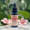 Facial oil bottle labeled 'GLOW' with pink flowers and green leaves in the background