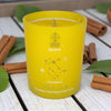Yellow candle with astrological design on a wooden surface with cinnamon sticks and leaves.