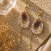 Pair of earrings with agate-like stones on a textured surface with dried flowers.