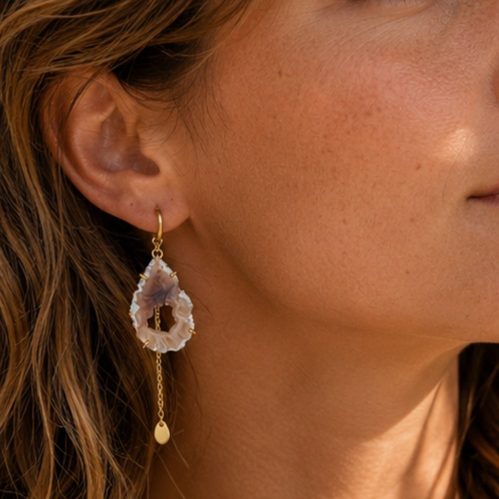 Close-up of a woman wearing a gold earring with a dangling gemstone.