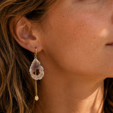 Close-up of a woman wearing a gold earring with a dangling gemstone.