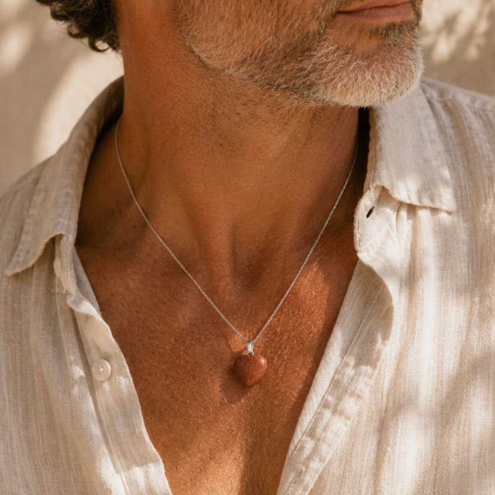 Man wearing a Goldstone Mini Heart Pendant necklace in warm natural sunlight.