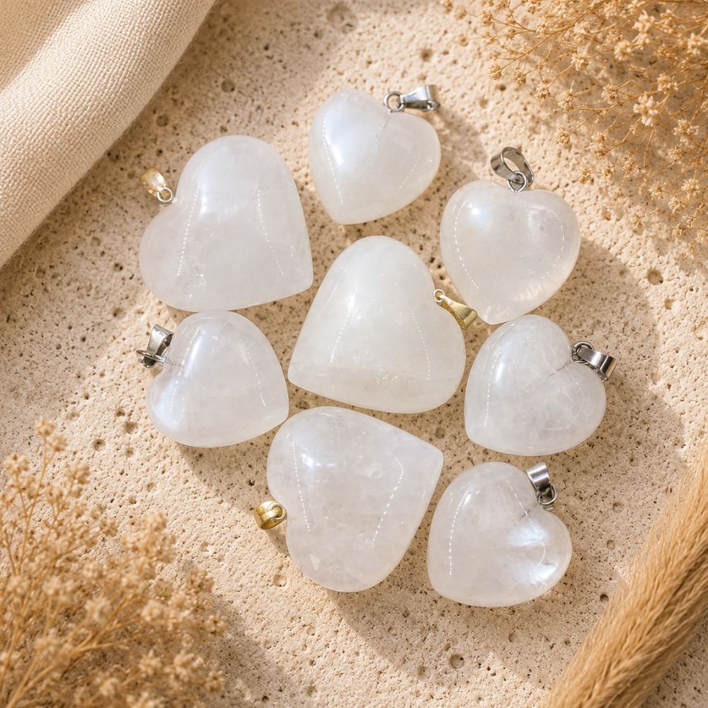 Snow Quartz heart crystal pendants with silver and gold bails on a neutral textured background.