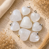 Snow Quartz heart crystal pendants with silver and gold bails on a neutral textured background.