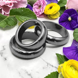 Three Hamatite rings arranged on a white marble surface with colorful flowers and green leaves around them.