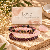 Three beaded gemstone bracelets arranged on a textured stone surface with a pink rose quartz crystal and a printed card reading 'Love' and 'Connect with the driving force of the Universe with these stones.' The bracelets include rhodonite, rose quartz and garnet.