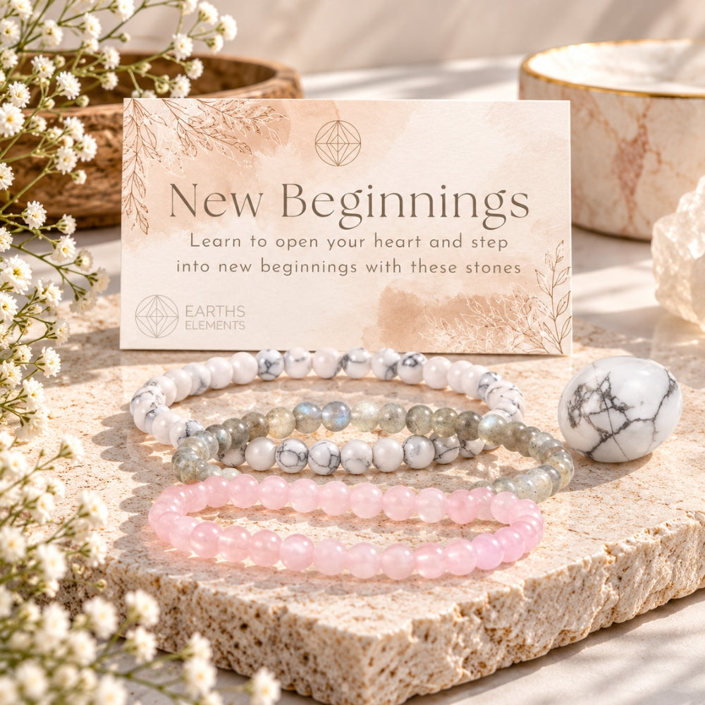 Three beaded stretch bracelets displayed on a stone slab with a branded card reading 'New Beginnings' and 'Earth's Gemstones.' The bracelets include howlite, labradorite, and rose quartz.