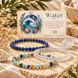 Three beaded stretch bracelets arranged on a burlap surface with a decorative card reading “Water” behind them. The bracelets include dark blue lapis lazuli, clear quartz, and amazonite.