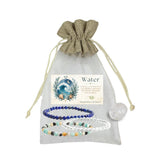 A beaded bracelet gift set labeled 'Water' displayed inside a sheer light gray drawstring pouch. The set includes a dark blue bead bracelet, a clear crystal bracelet, and a multicolor beaded bracelet, alongside a clear quartz tumble and an illustration card.