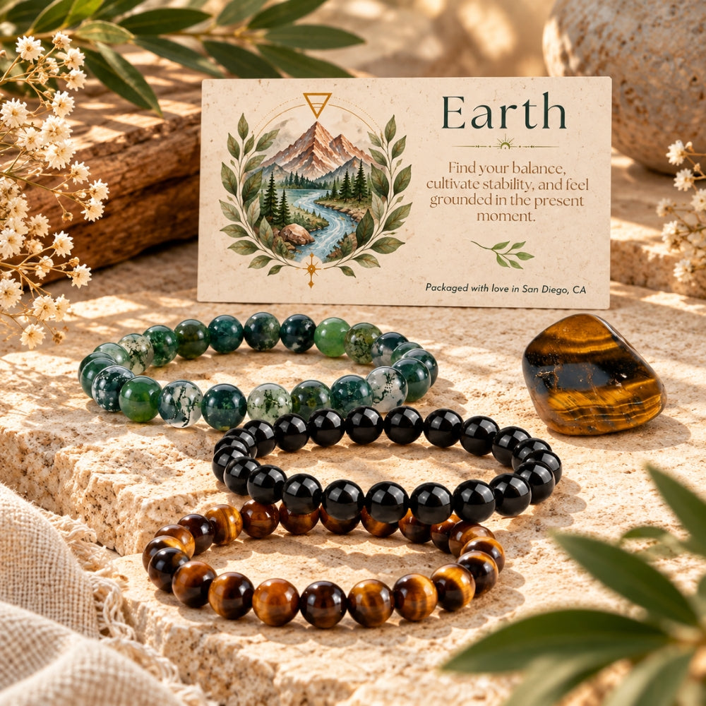 Three beaded stretch bracelets arranged on a stone surface with a small printed card behind them and a tiger's eye stone nearby. The bracelets are made of round beads they are moss agate, black obsidian, and tiger's eye.