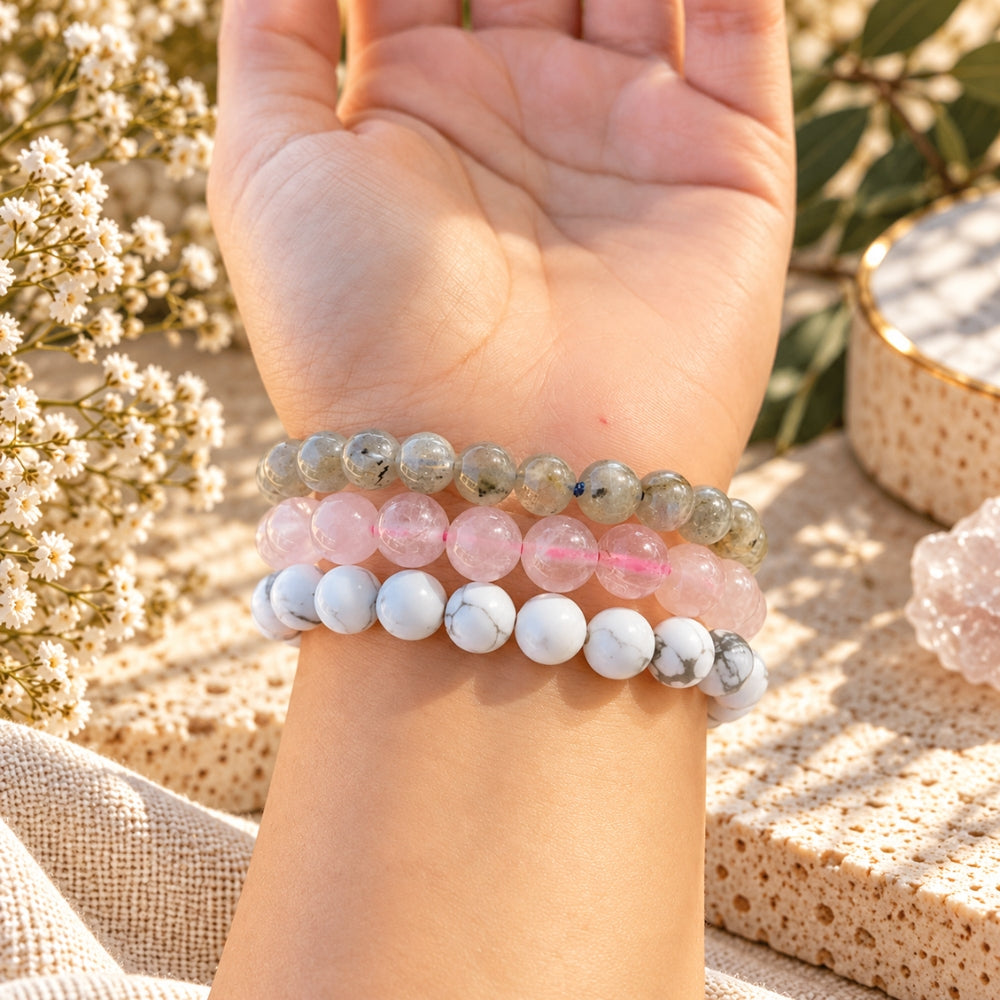 Three beaded stretch bracelets worn on a person's wrist, featuring howlite, labradorite, and rose quartz, displayed against a warm, boho-style background with dried flowers.