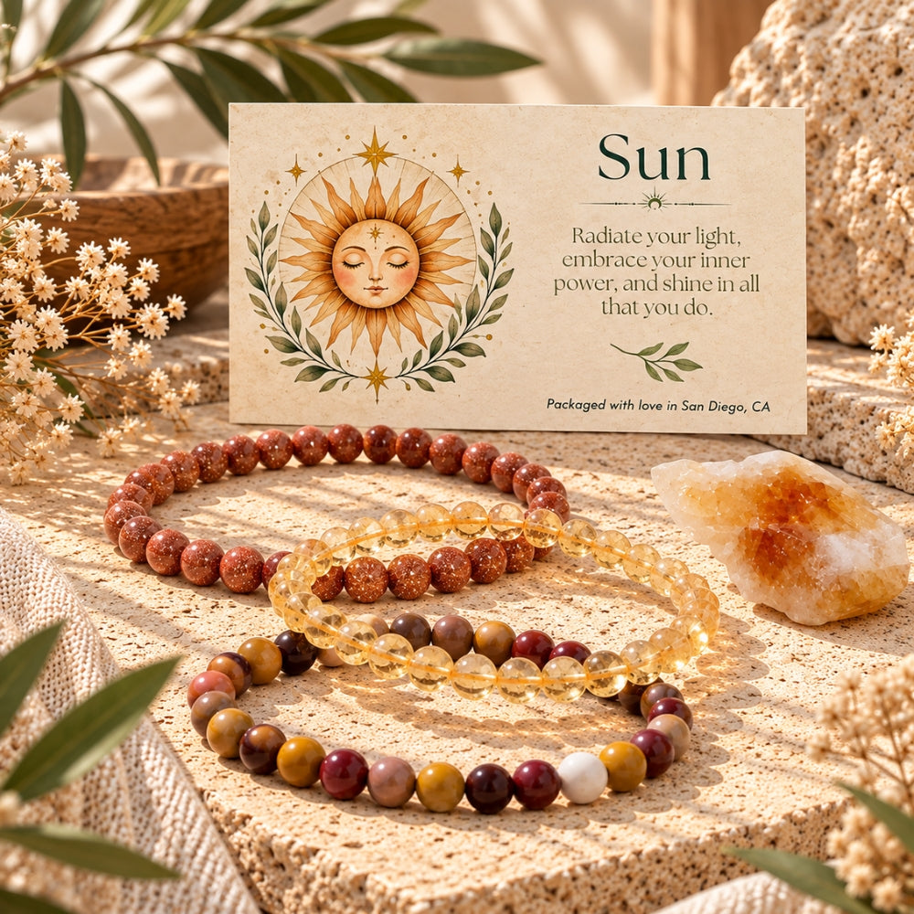 Three beaded stretch bracelets arranged on a textured stone surface beside a printed card labeled "Sun" with a sun illustration and quote. The bracelets include goldstone, citrine, and mookaite.