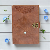 Brown leather notebook with embossed design and gold latch on a light wooden surface with blue flowers.