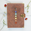 Brown leather journal with chakra design on a marble surface with flowers.