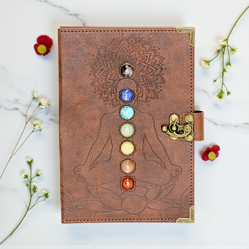 Brown leather journal with chakra design on a marble surface with flowers.