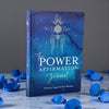Blue journal titled 'The Power Affirmation Journal' with decorative elements on a gray background.