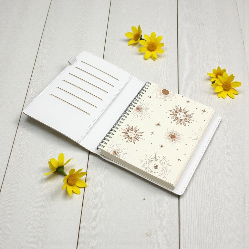 Open notebook with floral design on a light wooden surface with yellow flowers.