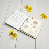 Open notebook with floral design on a light wooden surface with yellow flowers.