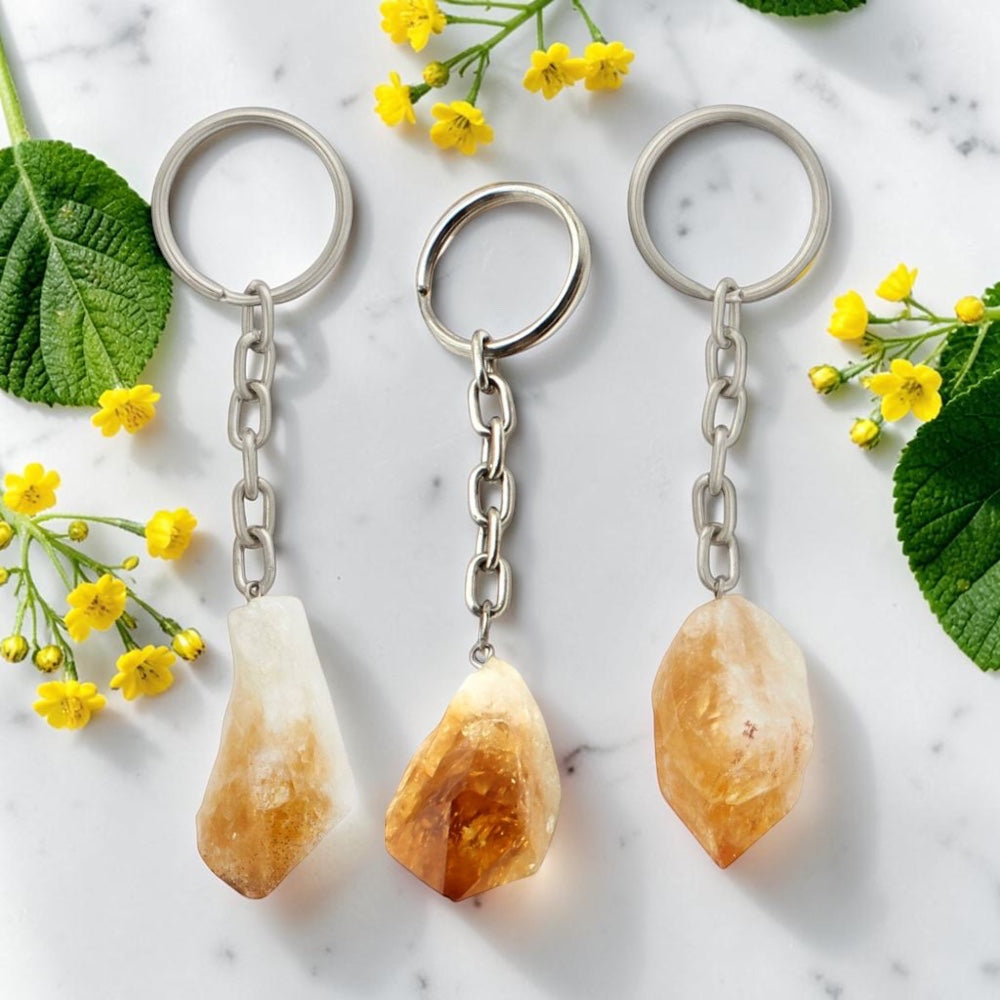 Three crystal keychains on a marble surface with yellow flowers and green leaves.