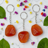 Three Carnelian keychains on a marble surface with flowers and leaves.